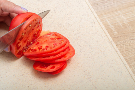 Red tomatoes are cut with a knife on a wooden board on the table. Medium shot.の写真素材