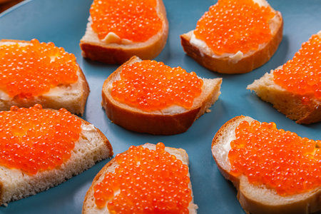 Canap s with red caviar and butter on a blue plate on a wooden table, close-up. Horizontal photo.の写真素材