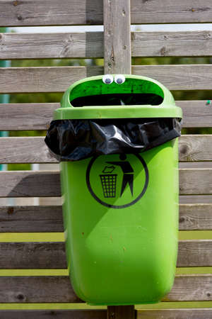 googly eyes on a green trash can mounted on a wooden fenceの写真素材