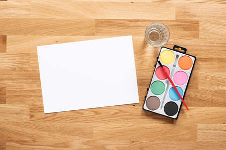Water colours, brush, water and a white paper on a wooden table.の写真素材