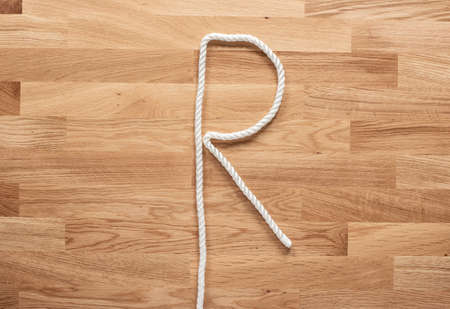 The letter R formed with white rope on a wooden tableの写真素材