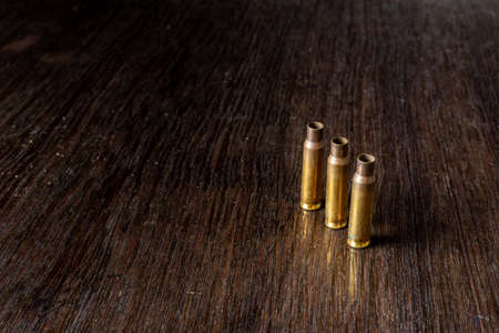 Empty bullet casings on a dark, wooden table.