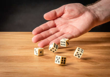 Hand throwing dice in front of a dark background.