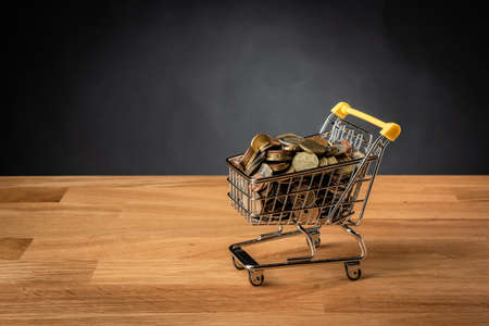Shopping cart filled with coins on a wooden table.の写真素材