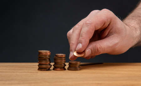 A hand stacking coins on a wooden table against a dark background.