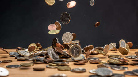 Different coins falling on a wooden table against a dark background.の写真素材