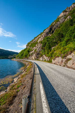Narrow, winding road by a fjord and steep cliffs above.の写真素材