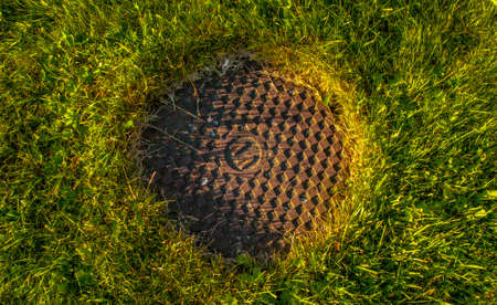 A rusty manhole cover in the middle of a grass field.の写真素材