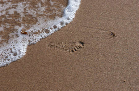 Footprint on a wet, sandy beach. Water is washing upp, about to erase the print.の写真素材