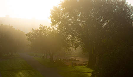 The sun shining throug dense morning fog over a playground.の写真素材