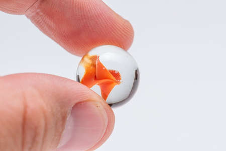Orange glass marble held by two fingersの写真素材