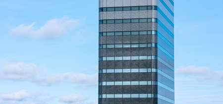 A tall, narrow high rise in gray against a blue and cloudy sky.