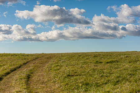 Faint tracks going up a grass hill. Cloudy but sunny sky.の写真素材