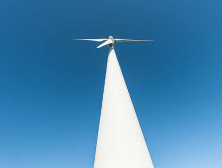 A tall, white wind turbine against a blue sky.