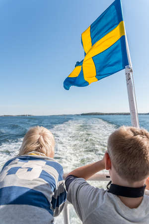 two Boys on a boat looking at the horizon. The swedish flag is waving in the breeze.の写真素材