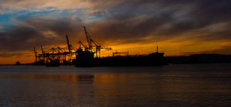 Silhouette of an oil tanker at sunset. Container port in the background.の写真素材