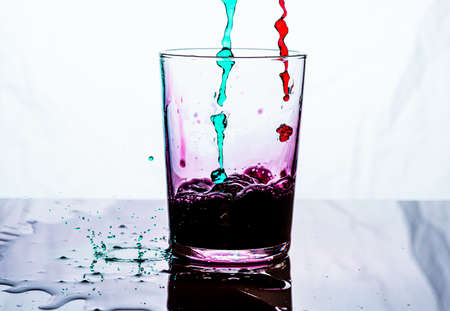 A glass being filled by pink and green liquid. White background..の写真素材