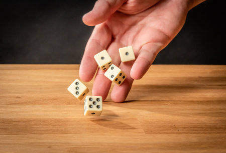 Hand throwing five dice on a wooden tableの写真素材
