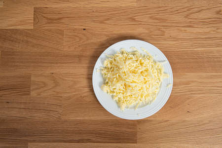 Plate of finely grated cheese on a wooden table.の写真素材