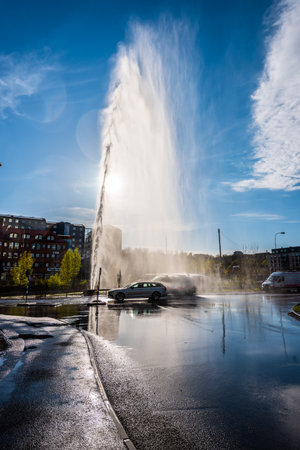 Gothenburg, Sweden - May 01 2022: Cars driving through a water filled street getting thoroughly washed by a large mains water leakのeditorial素材
