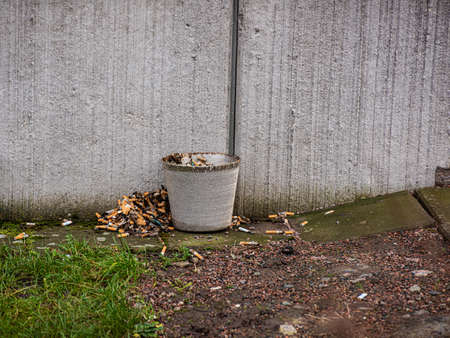 Small metal bucket with piles of cigarette buds both in and outsideの写真素材