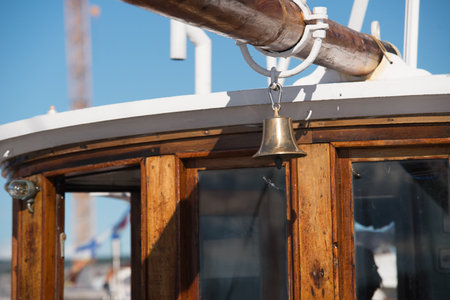 Bell hanging from the boom by the wheel house of a wooden shipの写真素材
