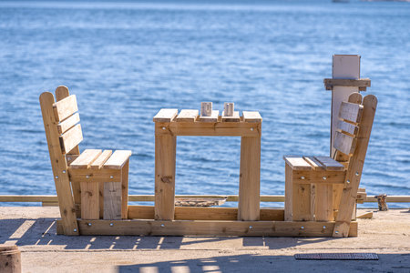 Two mugs on a table by benches by the seaの写真素材