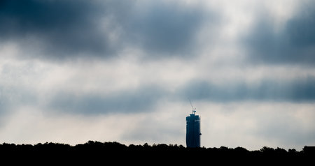 Silhouette of tall skyscraper under construction behind a forestの写真素材