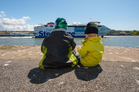Gothenburg, Sweden - June 02 2012: Two kids sitting on a pier by the river with car ferry passing in the backgroundのeditorial素材