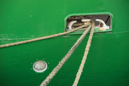 Roped going through a mooring hole of a green metal ship