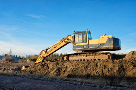 Yellow excavator on a road construction site against blue sky.