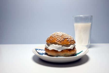 A traditional Scandinavian shrovetide bun with whipped cream, pearl sugar on top and a glass of milk on white table. Shrovetide buns are classic delicacies for Shorevetide Sunday and Tuesday.の写真素材