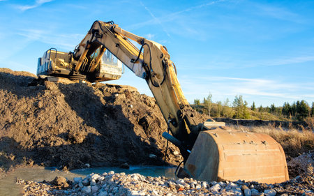 Yellow excavator on a road construction site against blue sky.の写真素材