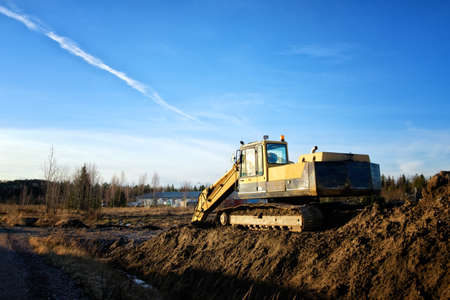 Yellow excavator on a road construction site against blue sky.の写真素材