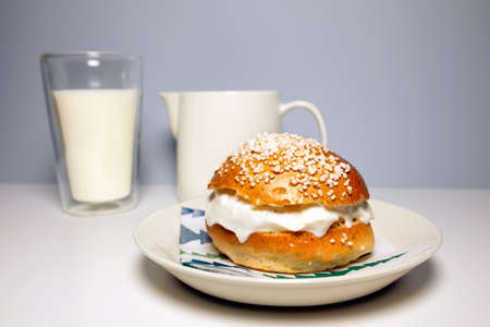 A traditional Scandinavian shrovetide bun with whipped cream, pearl sugar on top and a glass of milk on white table. Shrovetide buns are classic delicacies for Shorevetide Sunday and Tuesday.の写真素材