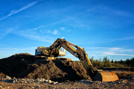 Yellow excavator on a road construction site against blue sky.の写真素材