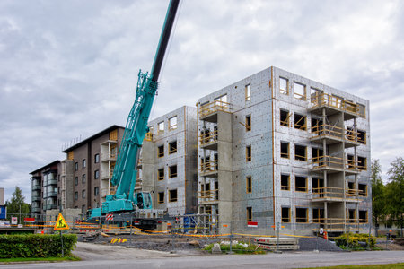 High rise building construction site with industrial mobile crane operating and lifting heavy loads on a cloudy day.の写真素材