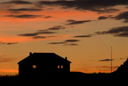 Silhouette of a lone house with a background of amazing skies lit by the setting sunの写真素材