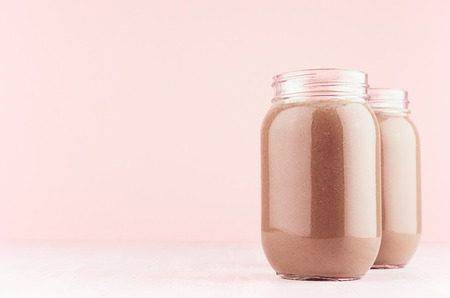 Chocolate milkshake in two stylish jars on white wooden table and pastel light pink wall.の写真素材