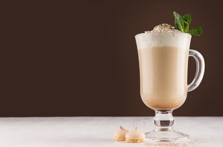 Coffee with cream, fresh mint, chocolate powder and cookies in irish coffee glass on dark brown and white wooden table, copy space.の写真素材