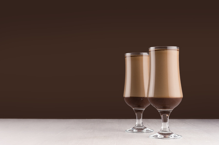 Creamy coffee cocktail in two elegant glass with chocolate on white table and dark brown wall.の写真素材