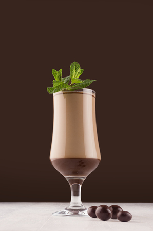Elegant chocolate striped dessert in wineglass with fresh green mint and with round chocolate candies on dark brown background, vertical.の写真素材
