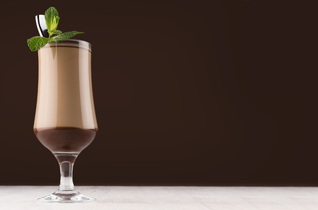 Chocolate milk cocktail in goblet with fresh green mint and silver spoon in elegant dark brown bar interior, copy space.の写真素材