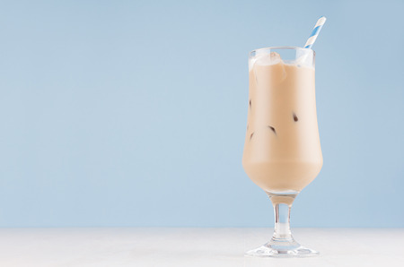 Creamy cold fresh beverage in elegant transparent glass with ice cubes and striped straw  in modern light blue interior, copy space.の写真素材