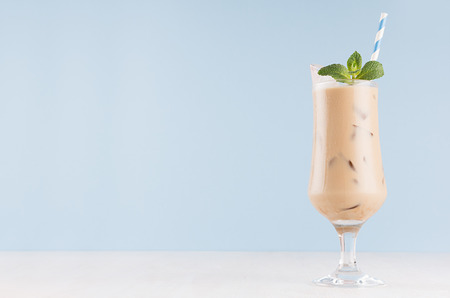 Fresh milk cocktail with coffee, green mint, ice cubes, and straw on light pastel blue wall and white wood board, copy space.の写真素材