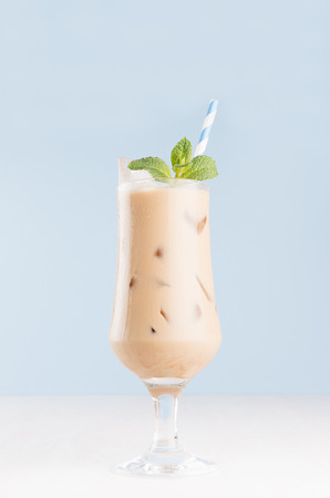 Refreshment baileys creamy cocktail in misted elegant wineglass with ice cubes, green mint, straw in light blue interior on white wooden table, vertical.の写真素材