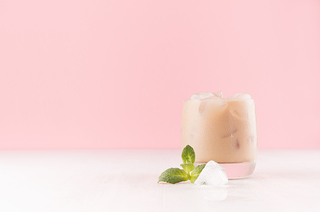 Fresh creamy alcoholic beverage with green mint, ice cube closeup in misted shot glass in pastel pink interior on white wooden table.の写真素材