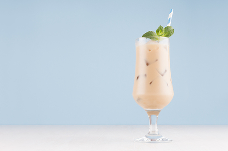 Summer ice coffee cocktail with green mint, ice cubes and striped straw on soft light blue wall and white wooden table, copy space.の写真素材