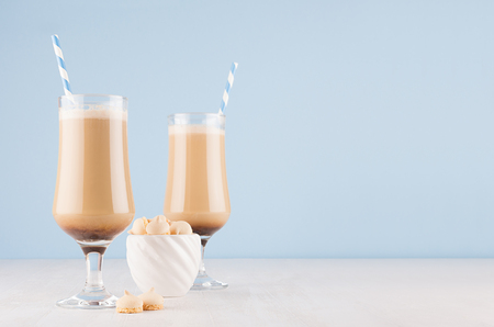 Fresh coffee drinks with cream, striped straws  in wineglass and cookies in bowl on soft light blue wall and white wooden table, copy space.の写真素材