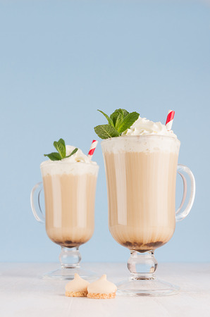 Refreshment coffee drinks with green fresh green mint, whipped cream, red striped straw, cookies in light blue interior on white wood table, vertical.の写真素材